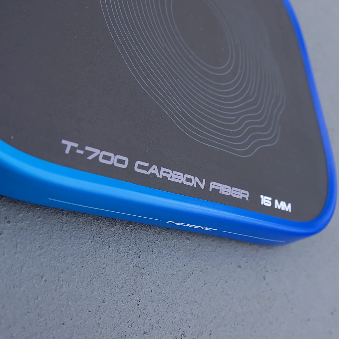 The raw carbon face of an AGOS paddle, close, with the printing along the edge