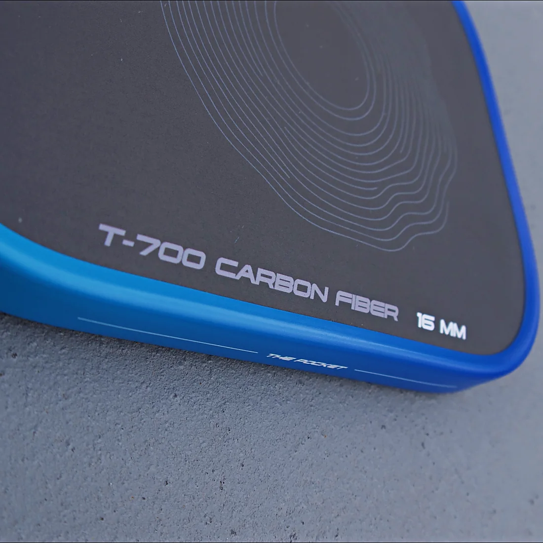 The raw carbon face of an AGOS paddle, close, with the printing along the edge