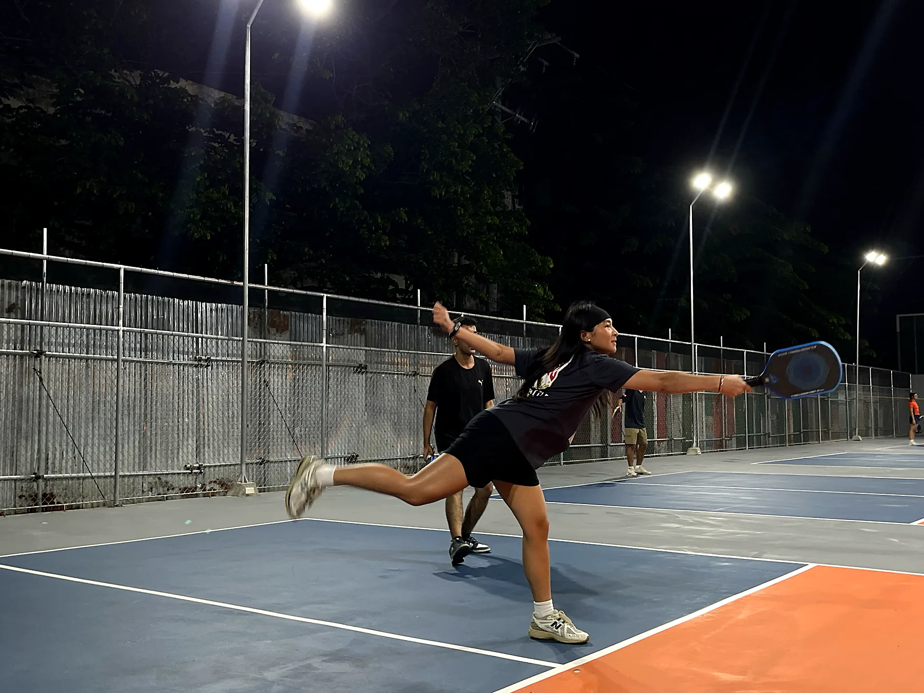 A player fully extended, running down a ball on a night court