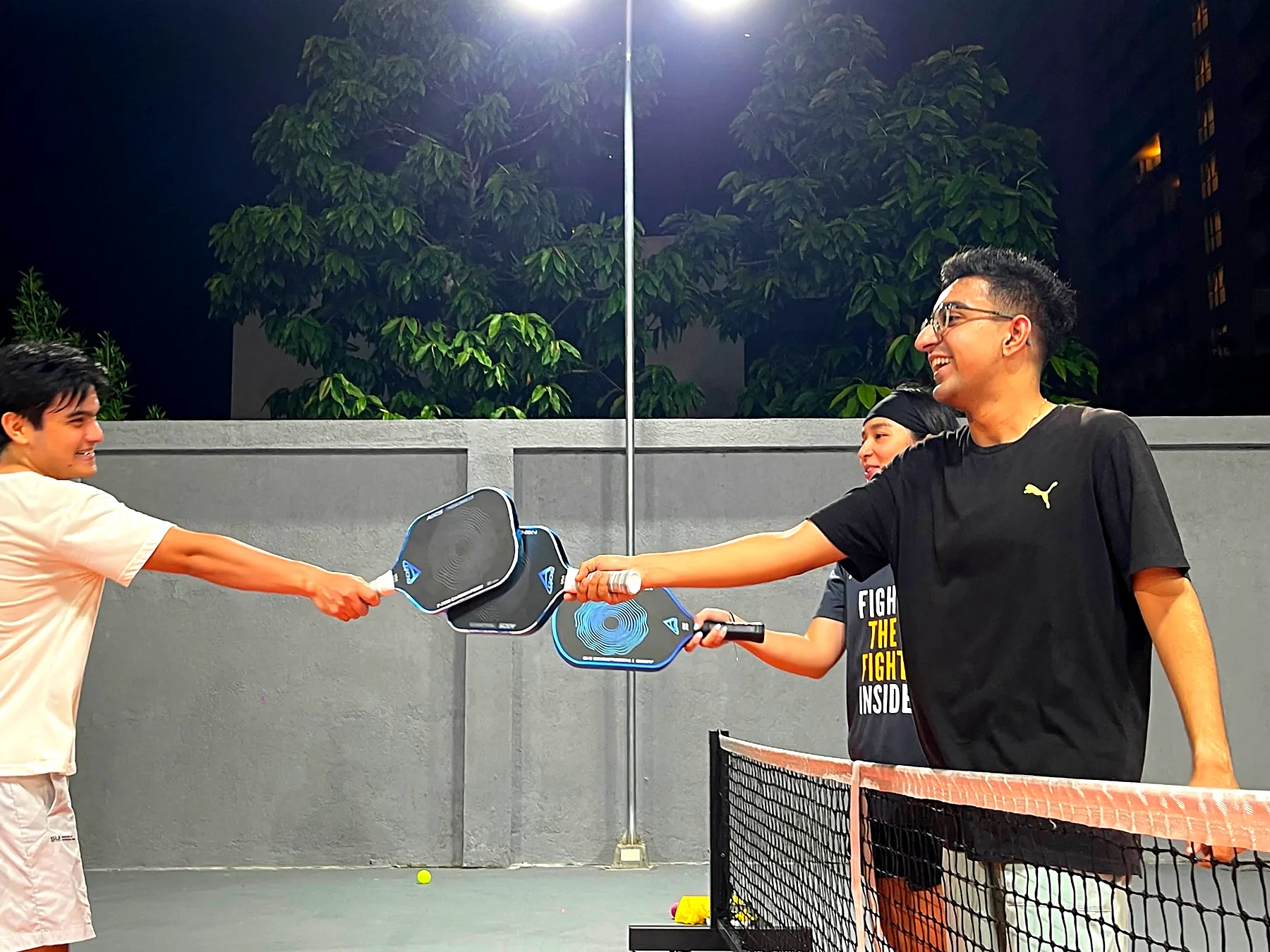 Two players tapping paddles over the net at the end of a game