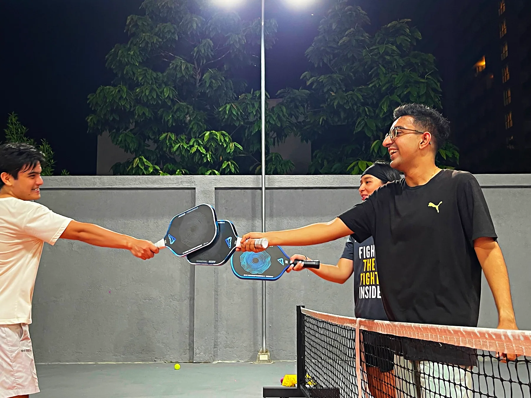 Two players tapping paddles over the net at the end of a game